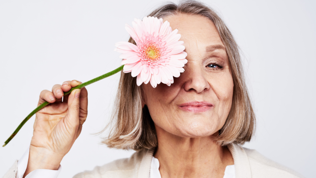 A woman with healthy bone density poses with a pink flower.